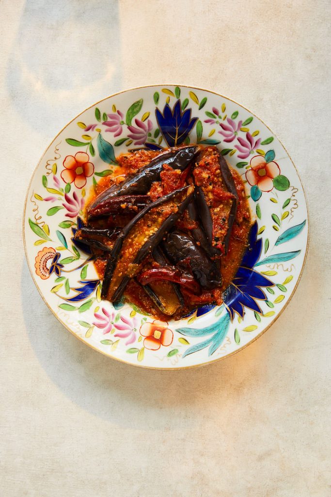 Bunter Teller mit gebratenen Auberginen in roter Sauce auf hellem Untergrund