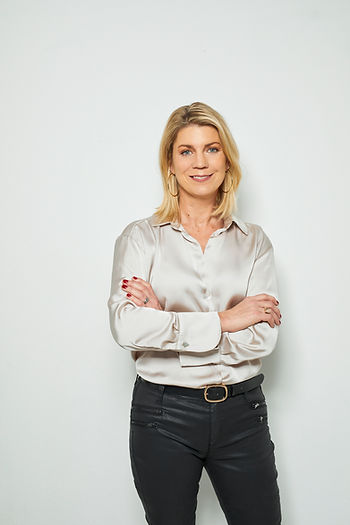 Catrin Marnitz mit schulterlangen blonden Haaren, die eine hell glänzende Bluse und schwarze Hose trägt und die Arme vor der Brust verschränkt hat