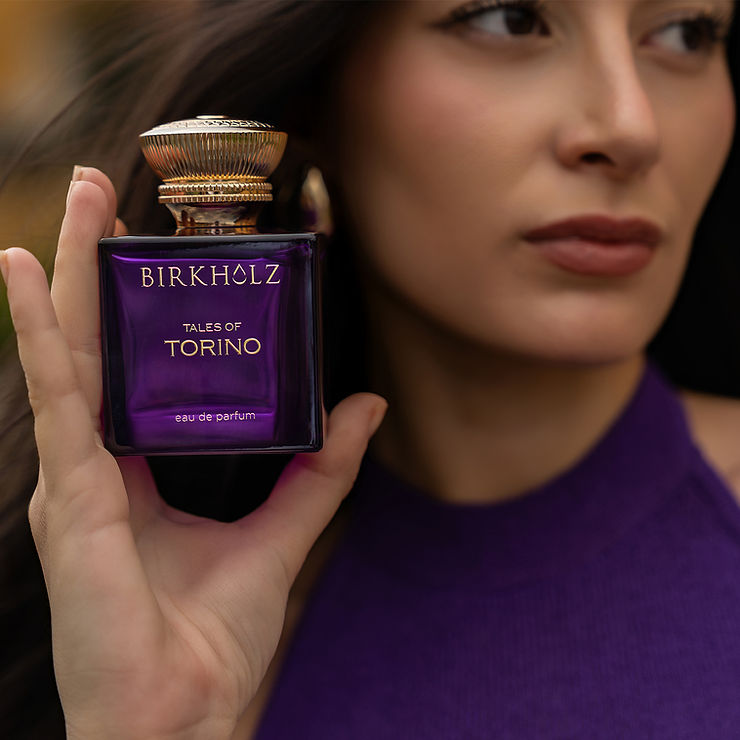 Hand hält eine lila Parfümflasche mit goldfarbenem Deckel und der Aufschrift 'BIRKHOLZ TALES OF TORINO eau de parfum'