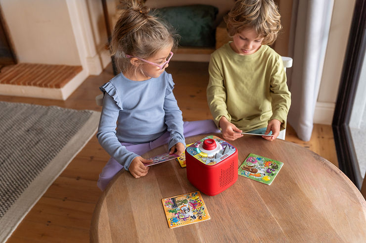 Zwei Kinder sitzen an einem runden Holztisch mit einem roten Spielgerät und mehreren Puzzleteilen
