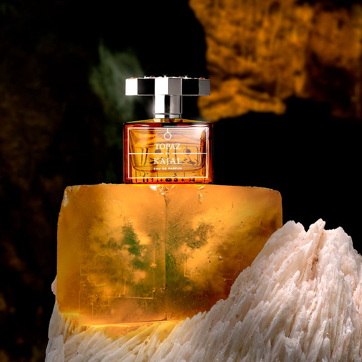 Flakon mit bernsteinfarbener Flüssigkeit und silber-schwarz kariertem Deckel steht auf einem großen bernsteinfarbenen Kristall neben einem weißen Kristall