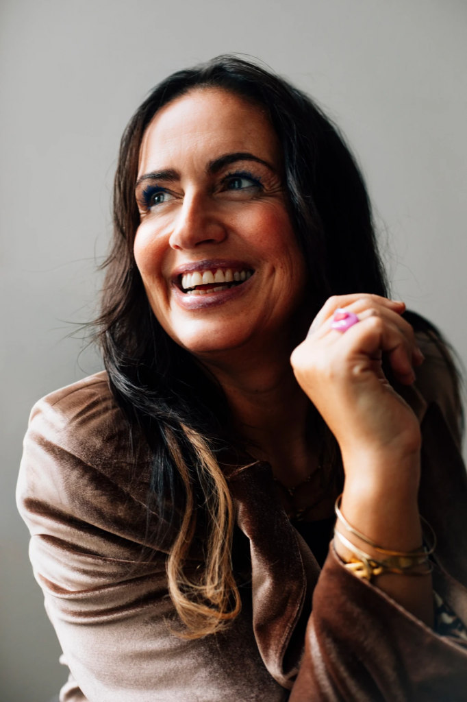 Sandra Günther mit langen dunklen Haaren trägt braune Jacke und mehrere Armbänder und hält die Hände vor dem Körper zusammen