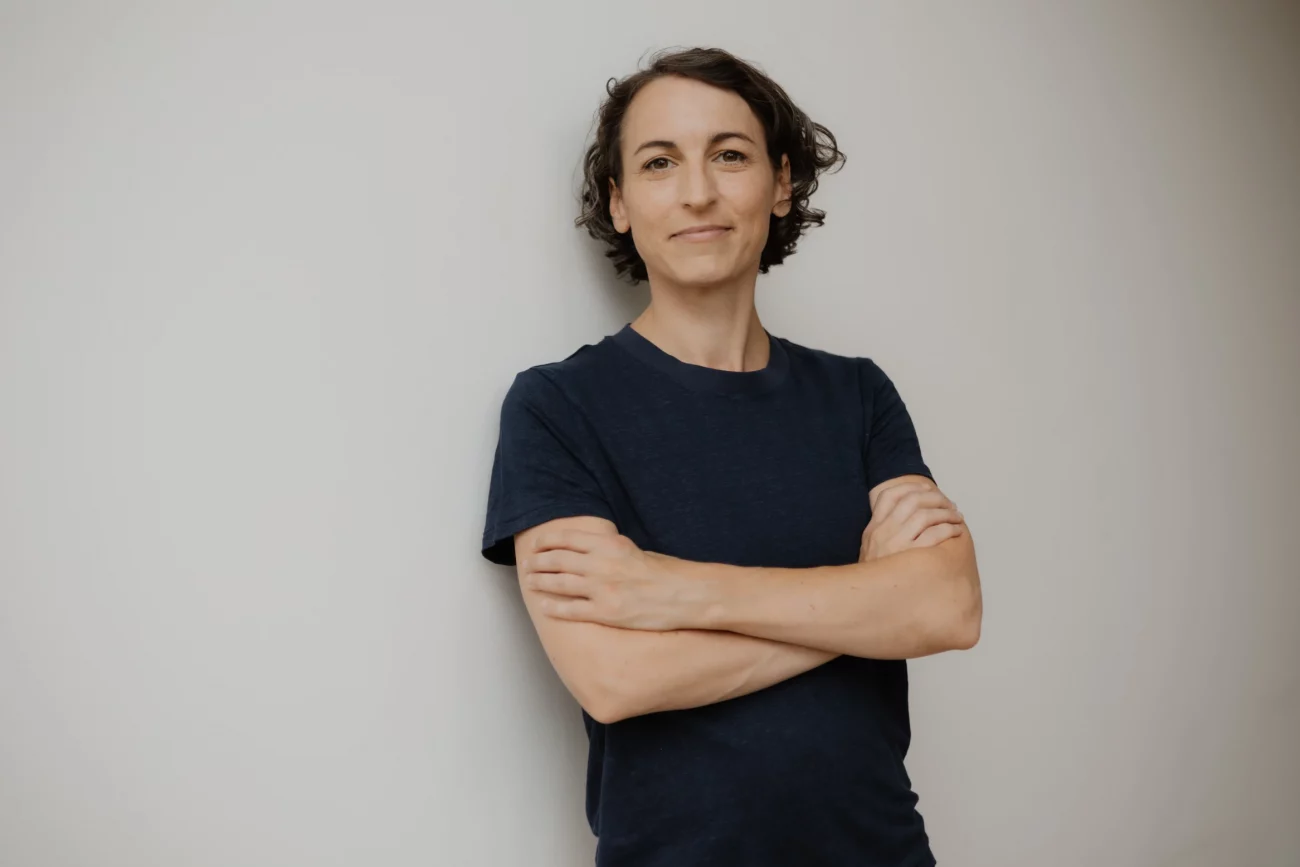 Natascha Wegelin mit verschränkten Armen vor weißer Wand in dunkelblauem T-Shirt