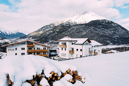 Schneebedeckte Holzhütte und Holzstapel vor schneebedecktem Bergpanorama