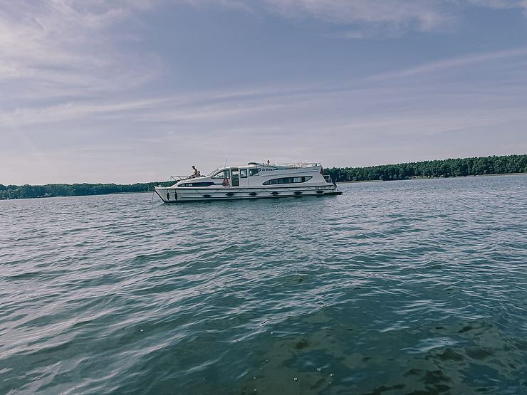 Ein weiße Jacht auf einem ruhigen See vor bewaldetem Ufer unter blauem Himmel
