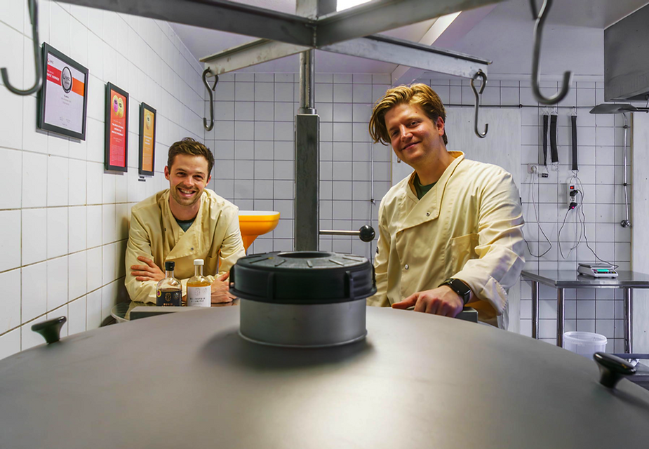 Zwei Personen in weißen Kitteln stehen in einem Raum mit weißen Kacheln und einem großen runden Metallgerät im Vordergrund