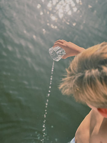 Von oben sichtbare Person mit kurzem Haar gießt Wasser aus einem Glas in ein Gewässer