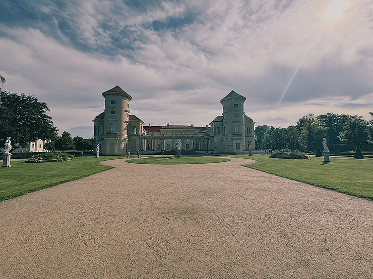 Schloss mit zwei runden Türmen und großem Vorplatz unter bewölktem Himmel