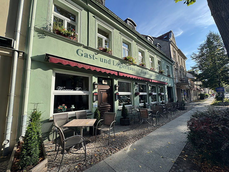 Fassade eines zweistöckigen Gasthauses mit Außentischen und Stühlen an einem sonnigen Tag