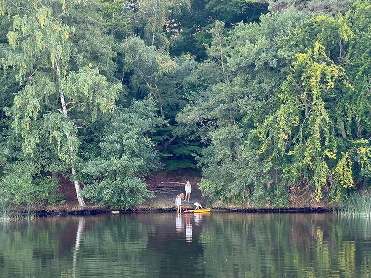 Drei Personen am Ufer eines Sees mit dichtem Baumbewuchs und einem gelben Kanu im Wasser