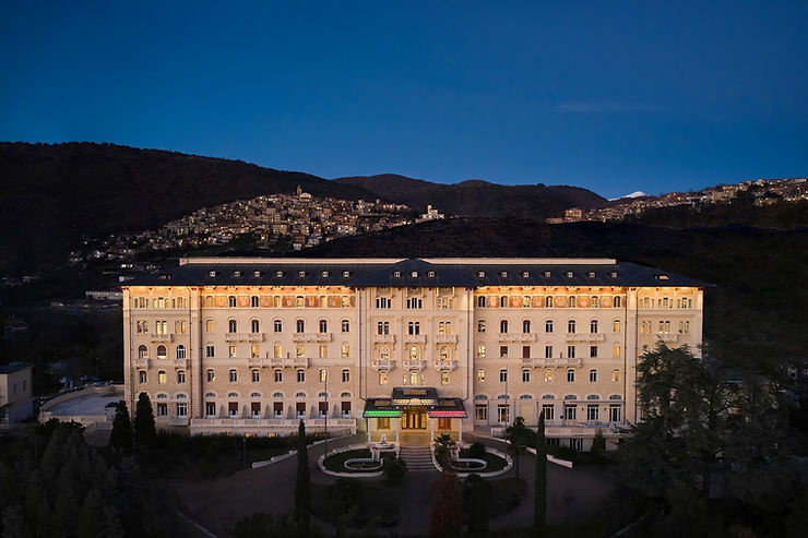 Beleuchtetes großes historisches Gebäude vor dunklem Bergpanorama in der Dämmerung