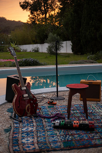 Halbakustische Gitarre, Mikrofonständer, Verstärker und Effektpedale auf einem gemusterten Teppich neben einem Pool bei Sonnenuntergang