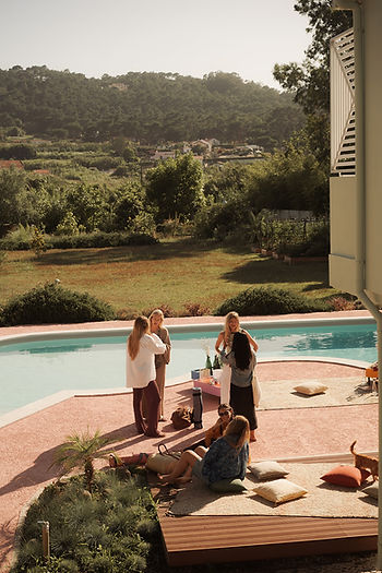 Gruppe von Menschen steht und sitzt auf einer Terrasse neben einem Pool mit Blick auf bewaldete Hügel