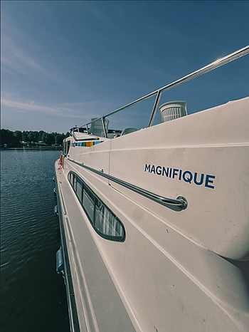 Seitenansicht eines weißen Bootes mit dem Schriftzug 'MAGNIFIQUE' am Bug und Wasser im Hintergrund
