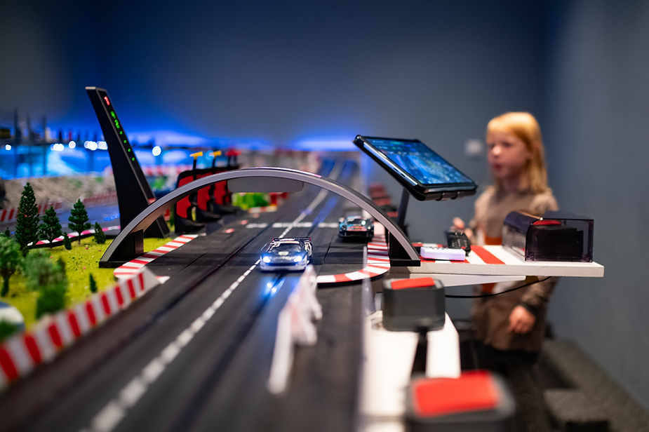 Modellrennstrecke mit zwei Spielzeugautos auf der Fahrbahn und einem Bogenbrücken-Element im Vordergrund