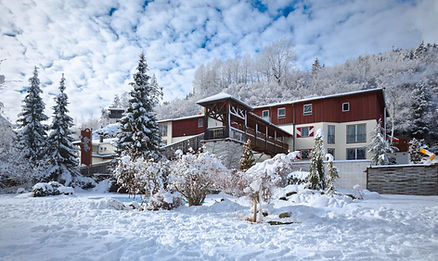 Schneebedecktes Hotelgebäude mit verschneiten Bäumen und Hügeln im Hintergrund