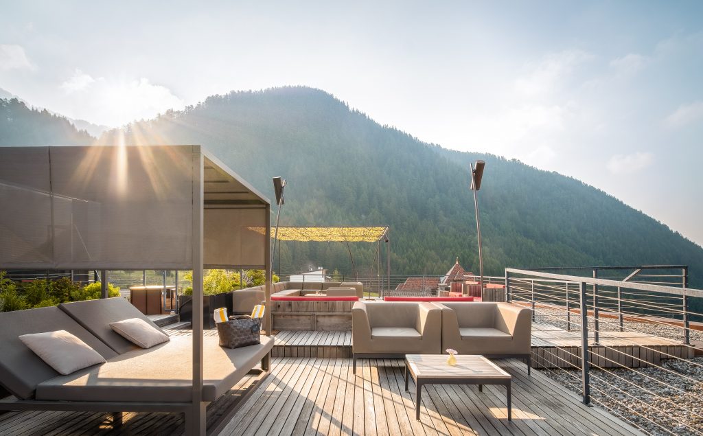 Terrasse mit Liegen, Sofas und Tisch vor bewaldetem Berg im Sonnenlicht