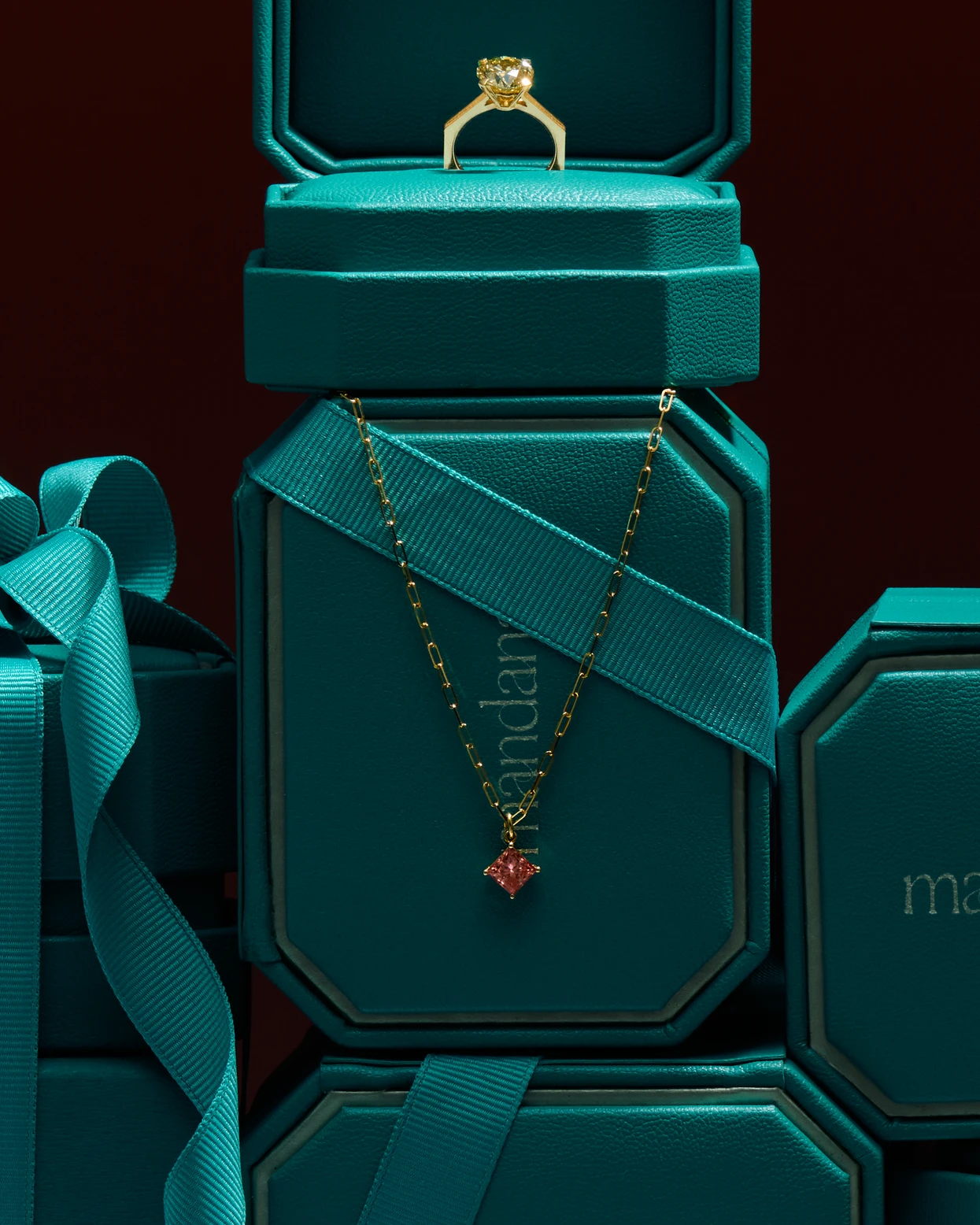 Goldener Ring mit Diamant in grünem Schmuckkästchen und goldene Kette mit rotem Anhänger auf grünem Hintergrund