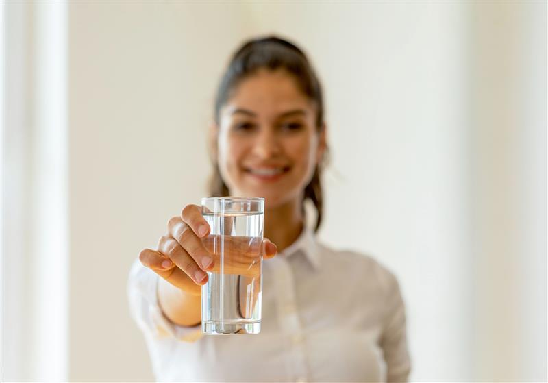 Frau in weißem Hemd hält ein Glas mit klarem Wasser nach vorne