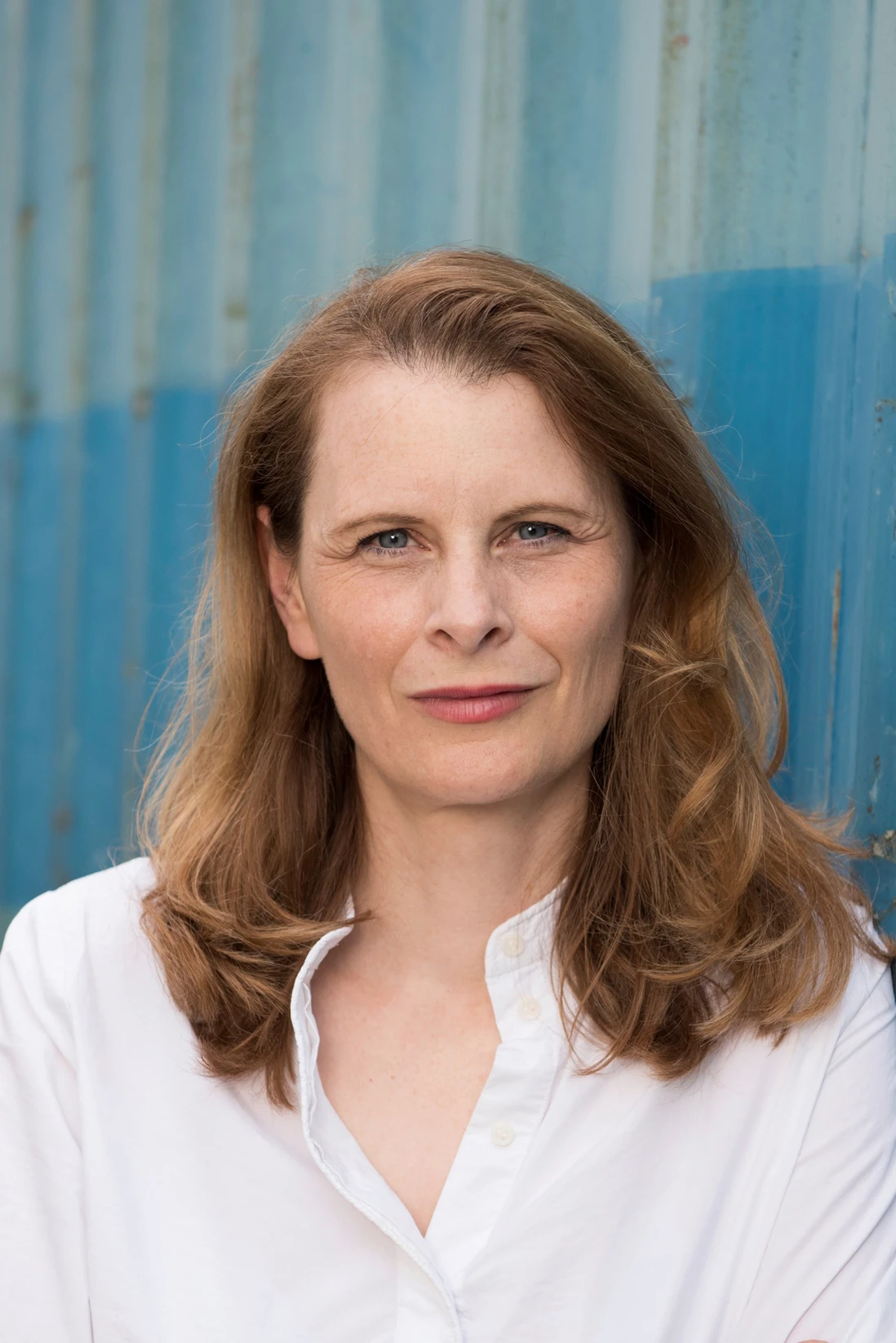 Heike Kleen mit schulterlangen, gewellten Haaren trägt ein weißes Hemd vor einer blau gestrichenen Wand