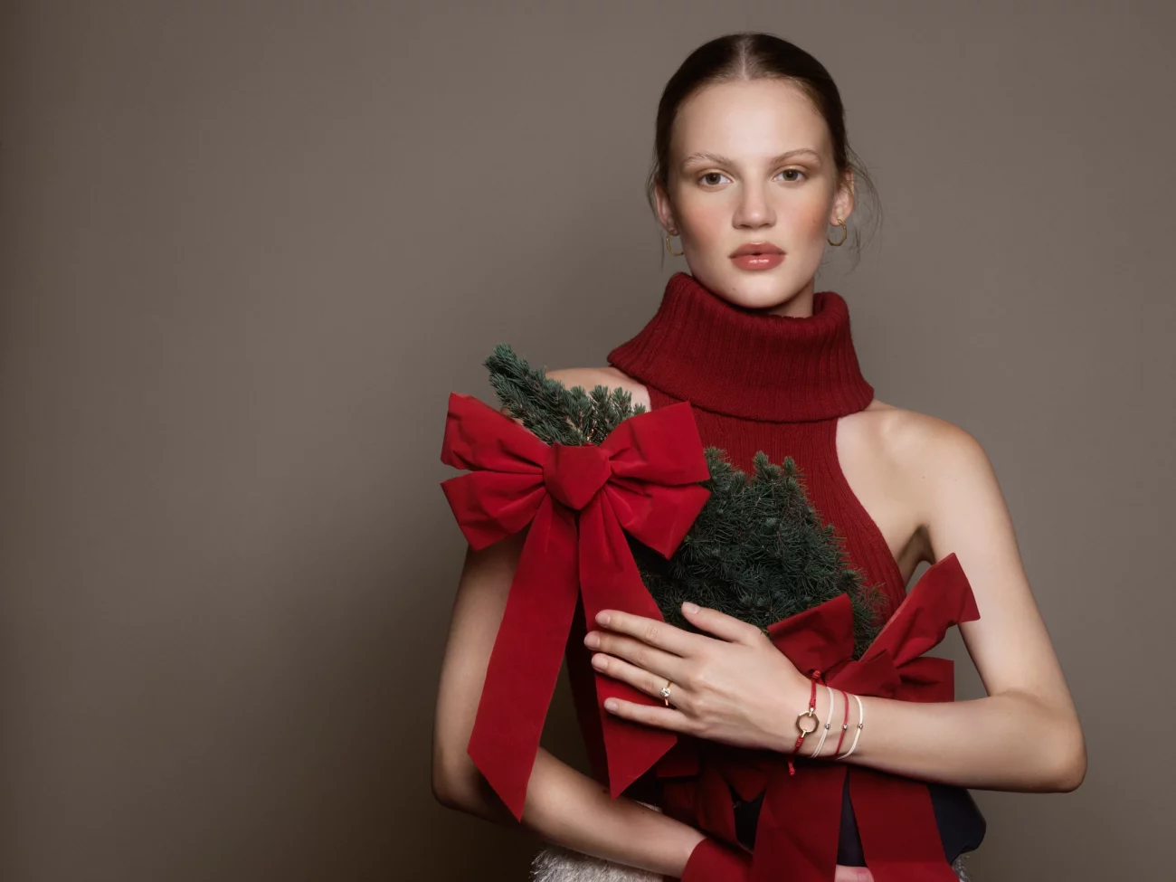 Frau in rotem Rollkragenpullover hält zwei kleine Tannenzweige mit großen roten Schleifen