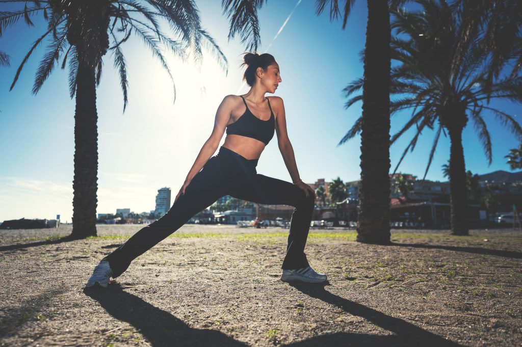 Melissa Khalaj in Sportkleidung macht Ausfallschritt im Freien vor Palmen bei Sonnenlicht
