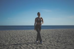 Melissa Khalaj in Sportkleidung geht auf einem Sandstrand mit Meer im Hintergrund