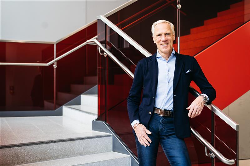 Ingo Froböse lehnt an einem Treppengeländer vor einer rot gestrichenen Wand