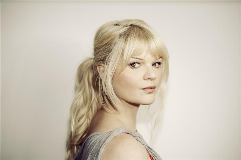 Sophie Passmann mit langem, gewelltem, blondem Haar im Pferdeschwanz, seitlich aufgenommen, trägt ein graues Oberteil