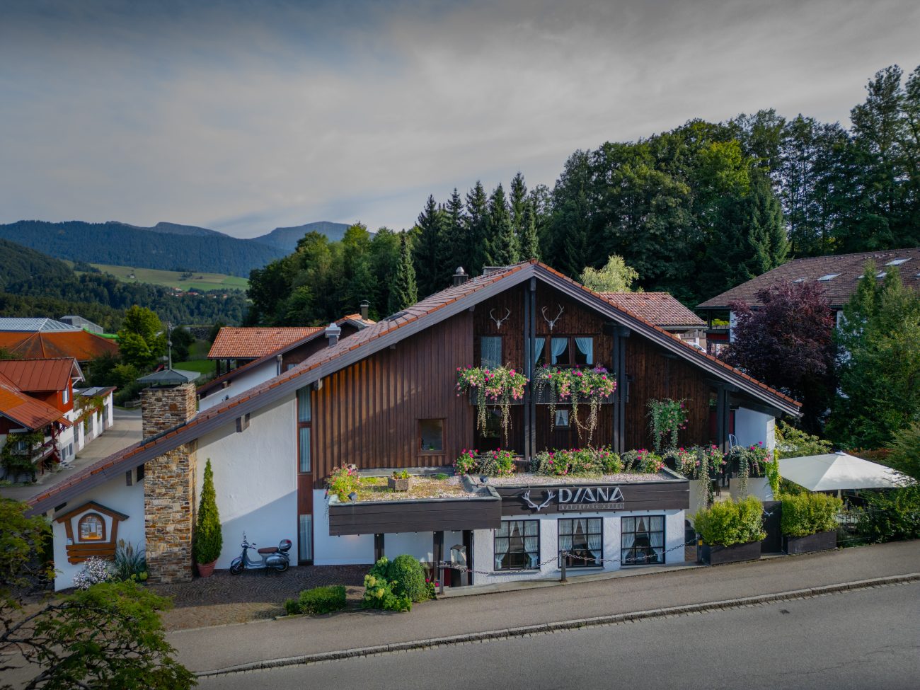 Traditionelles Hotelgebäude mit Holzbalkon und Blumenschmuck im Allgäu vor bewaldeten Hügeln