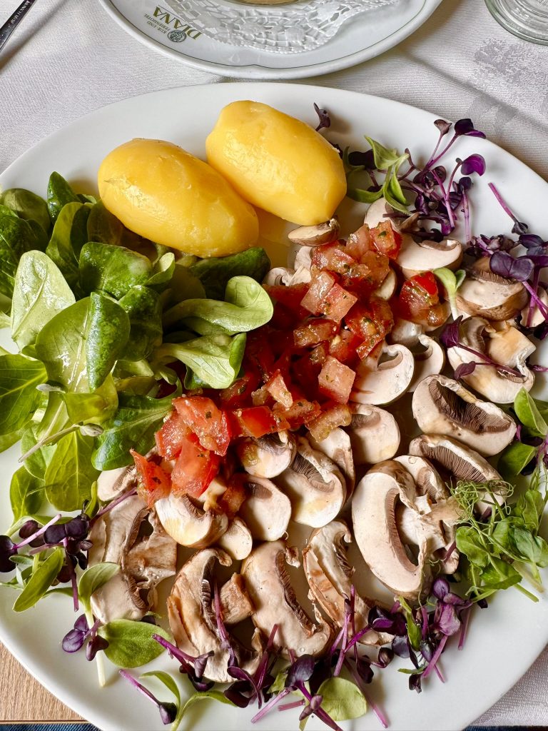 Teller mit zwei Kartoffeln, geschnittenen Champignons, gewürfelten Tomaten, Feldsalat und Mikrogrün.