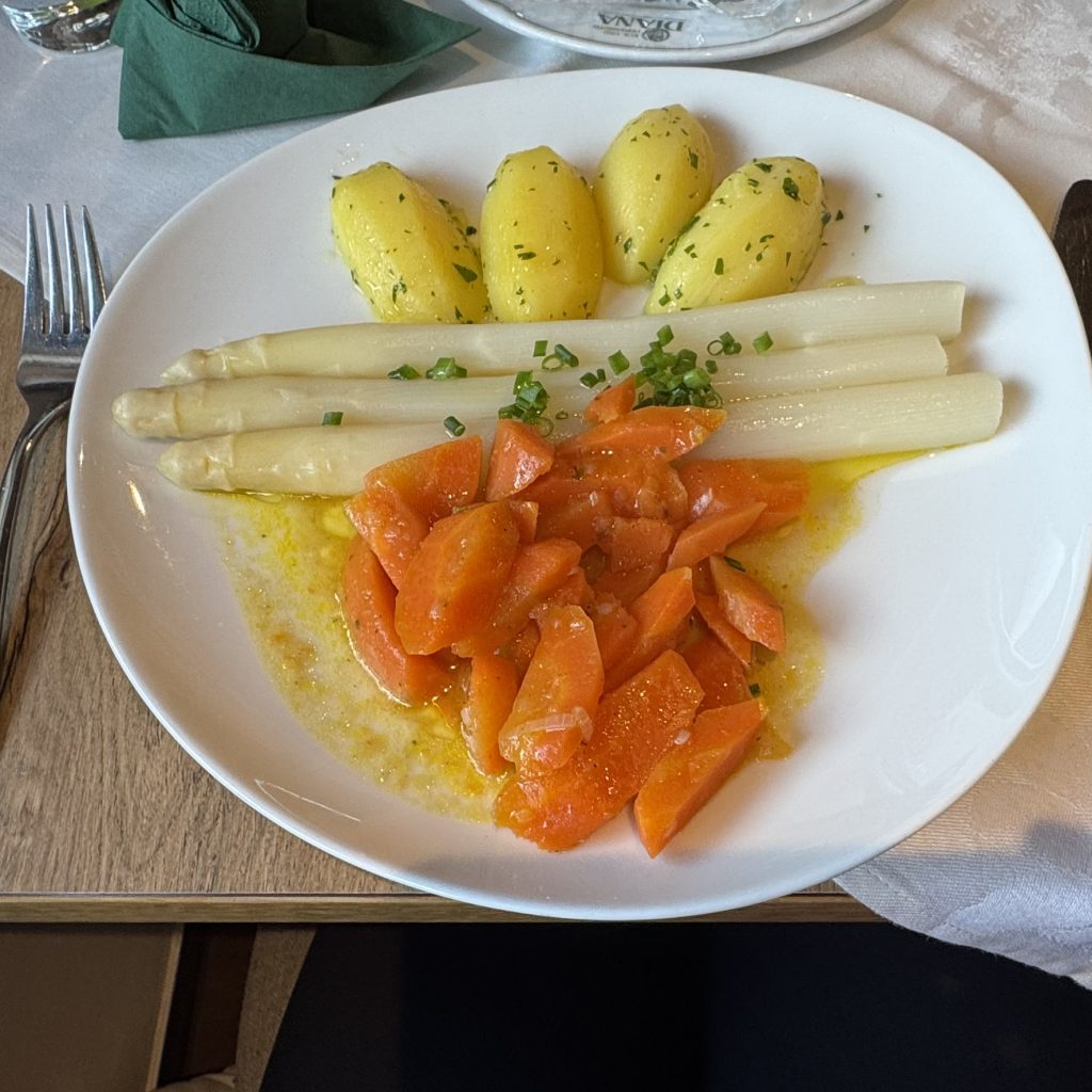 Weißer Spargel mit kleinen Salzkartoffeln und in Scheiben geschnittenen Karotten auf weißem Teller mit Butter und Schnittlauch.