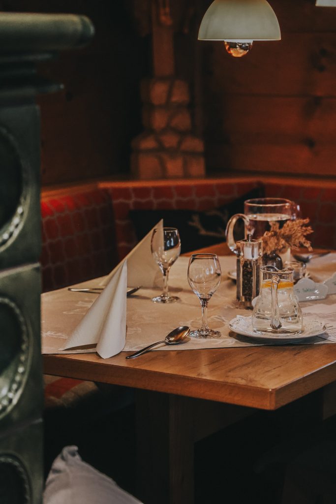 Holztisch in einem Restaurant mit eingedeckten Gläsern, Besteck, Servietten und einer kleinen Vase mit Trockenblumen