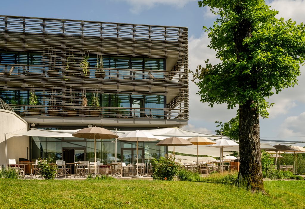 Moderner mehrstöckiger Gebäudekomplex mit großen Glasfronten und Sonnenschirmen auf der Terrasse