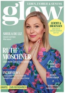 Ruth Moschner mit blonden Haaren in blauem Kleid mit pinken Blumen vor grünem Hintergrund mit Magazinüberschriften