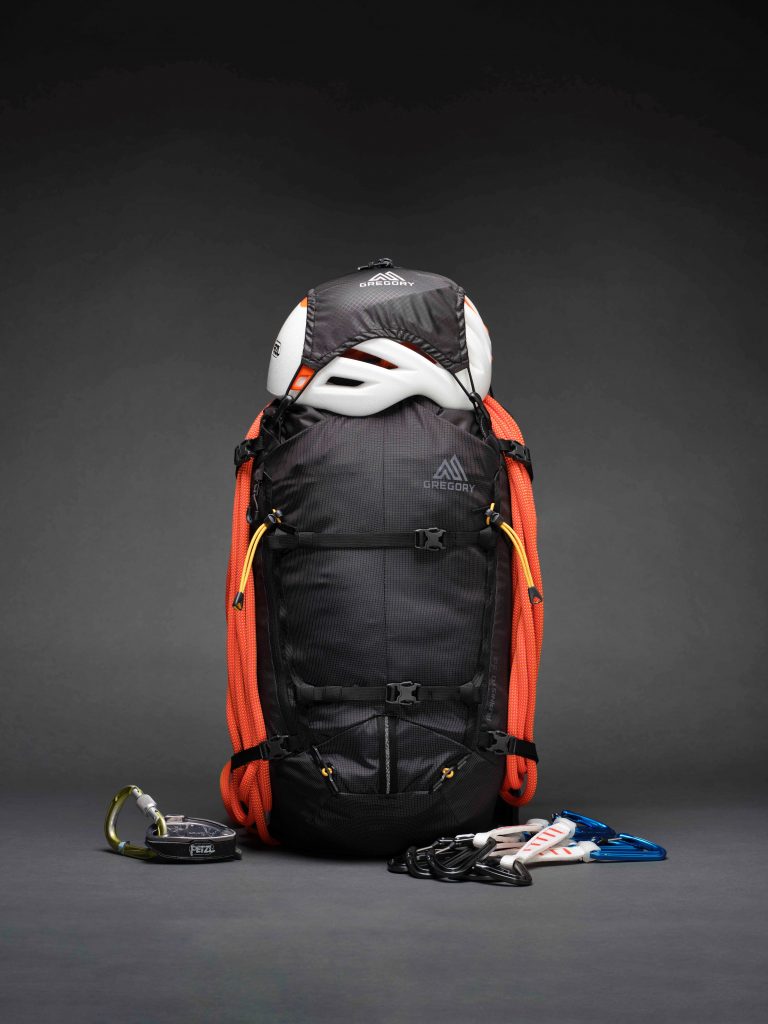 Schwarzer Rucksack mit orangefarbenem Kletterseil, weißem Helm und Kletterausrüstung vor dunklem Hintergrund