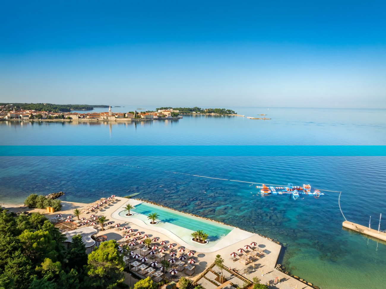 Infinity-Pool mit Liegen und Sonnenschirmen an der Küste mit Blick auf das Meer und eine entfernte Stadt
