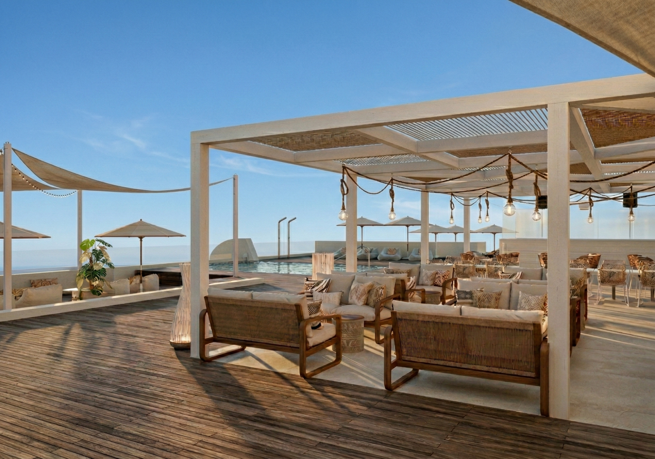 Offener Lounge-Bereich mit Holzterrasse, überdachten Sitzgruppen mit Polstermöbeln und Blick auf das Meer unter klarem Himmel
