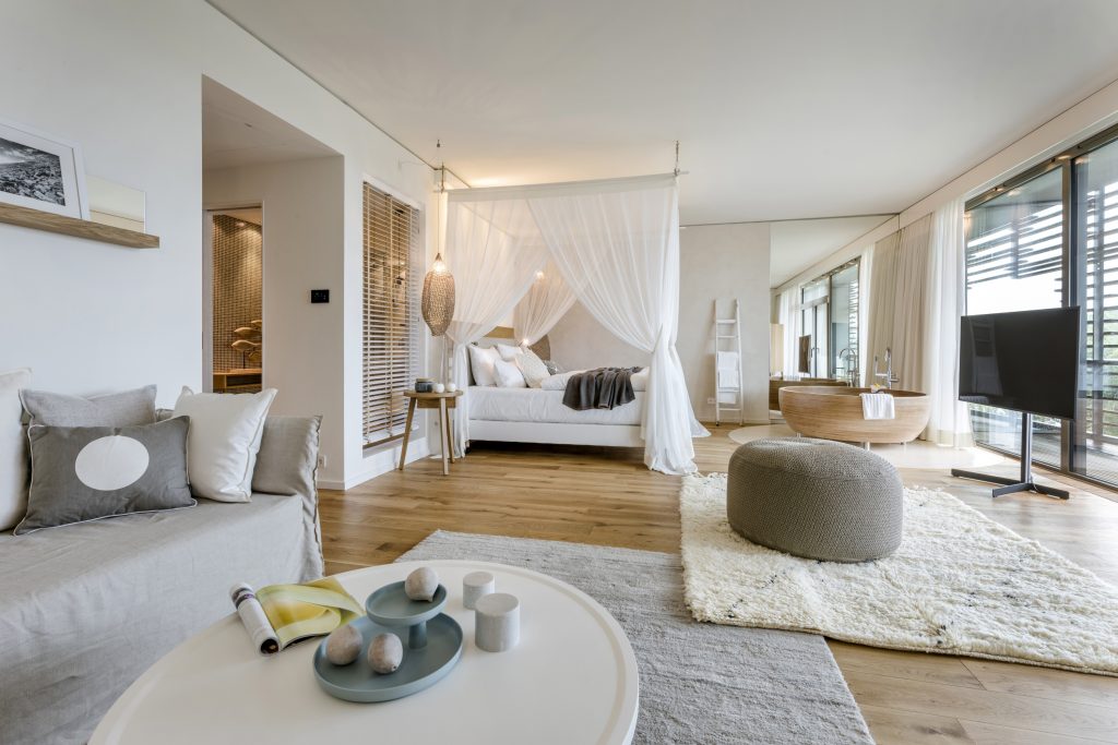 Helles Hotelzimmer mit Himmelbett, Sofa, runden Hockern und großem Fenster