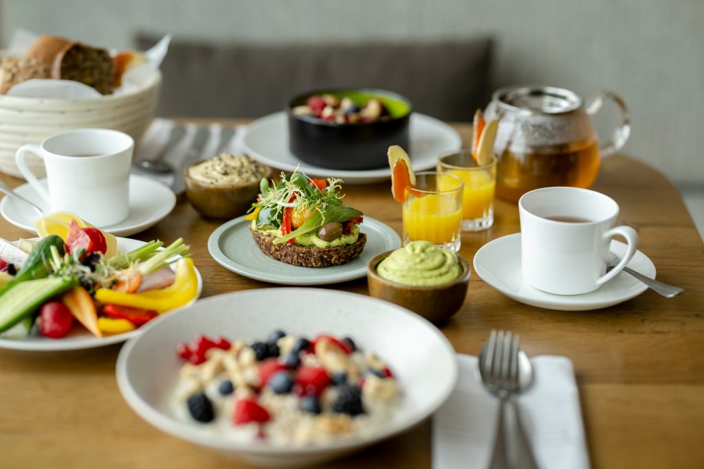 Frühstückstisch mit Vollkornbrot, Avocado, Müsli mit Beeren, Kaffee und Orangensaft