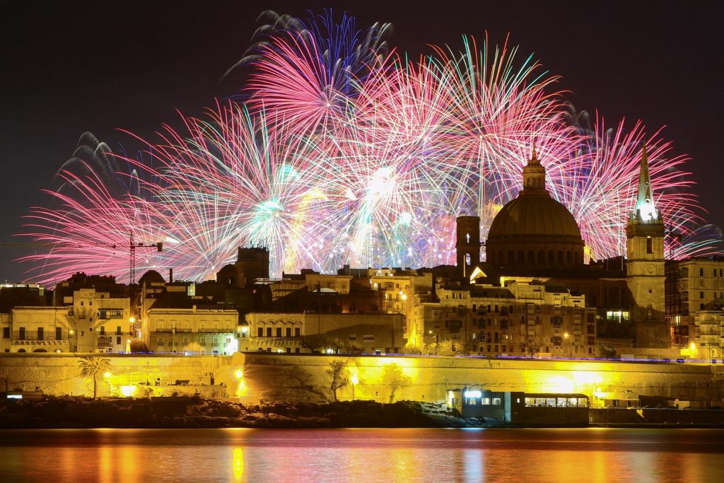 Feuerwerk über der beleuchteten Silhouette von Valletta mit markanter Kuppel und Kirchturm am Wasser