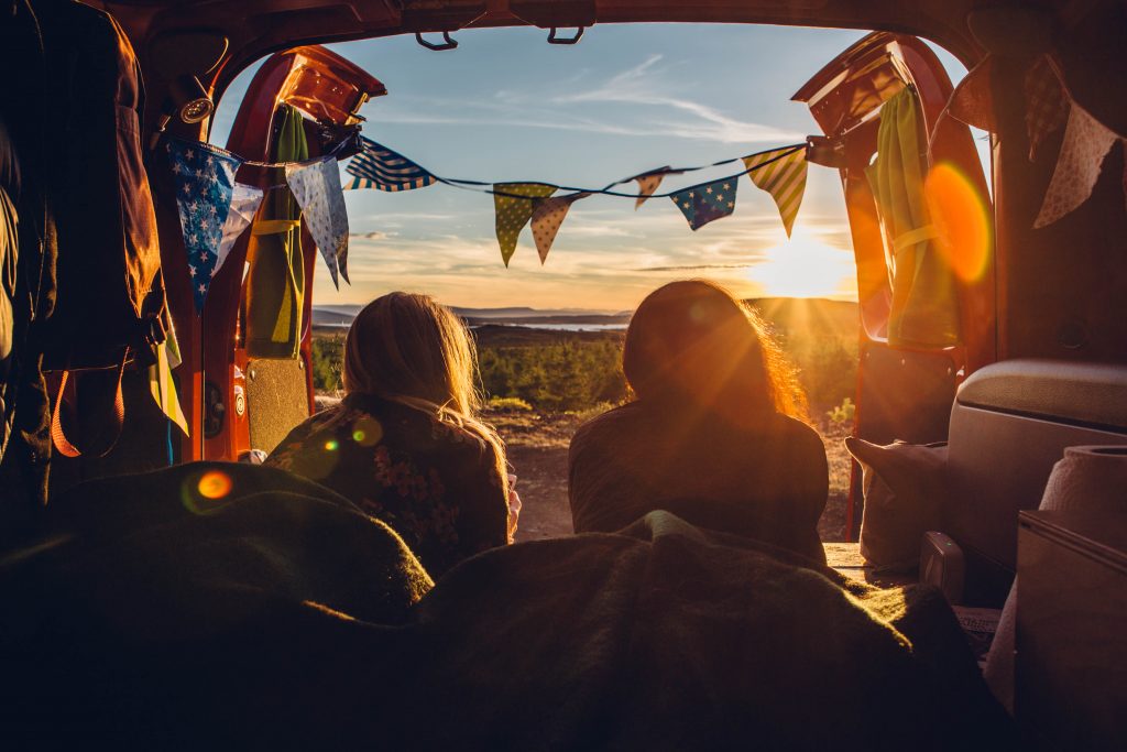 Rückansicht von zwei Frauen, die in einem offenen Wohnmobil liegen und den Sonnenuntergang betrachten