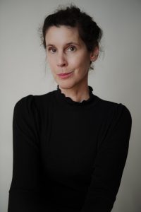 Daniela Dröscher mit zusammengebundenem dunklem Haar trägt schwarzen Pullover und blickt leicht lächelnd in die Kamera