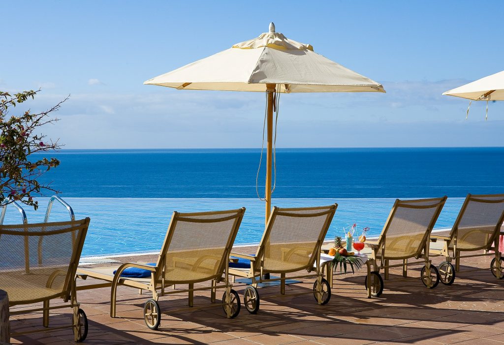 Reihe von Liegestühlen mit Sonnenschirmen auf einer Terrasse mit Blick auf das Meer