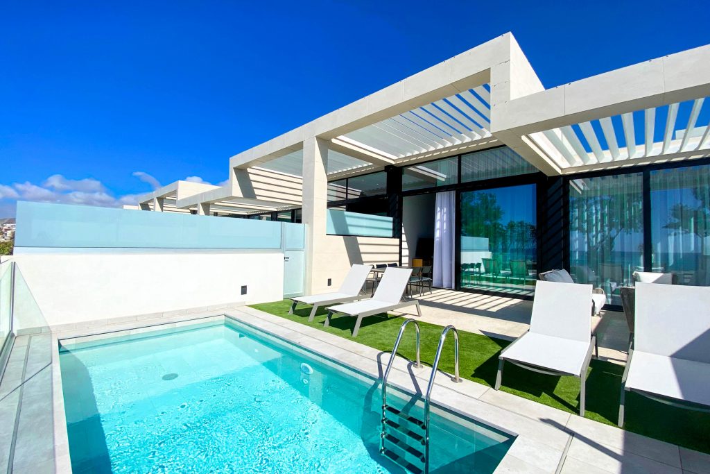 Moderner Außenbereich mit kleinem Pool, Liegestühlen und Pergola vor großen Glasfenstern