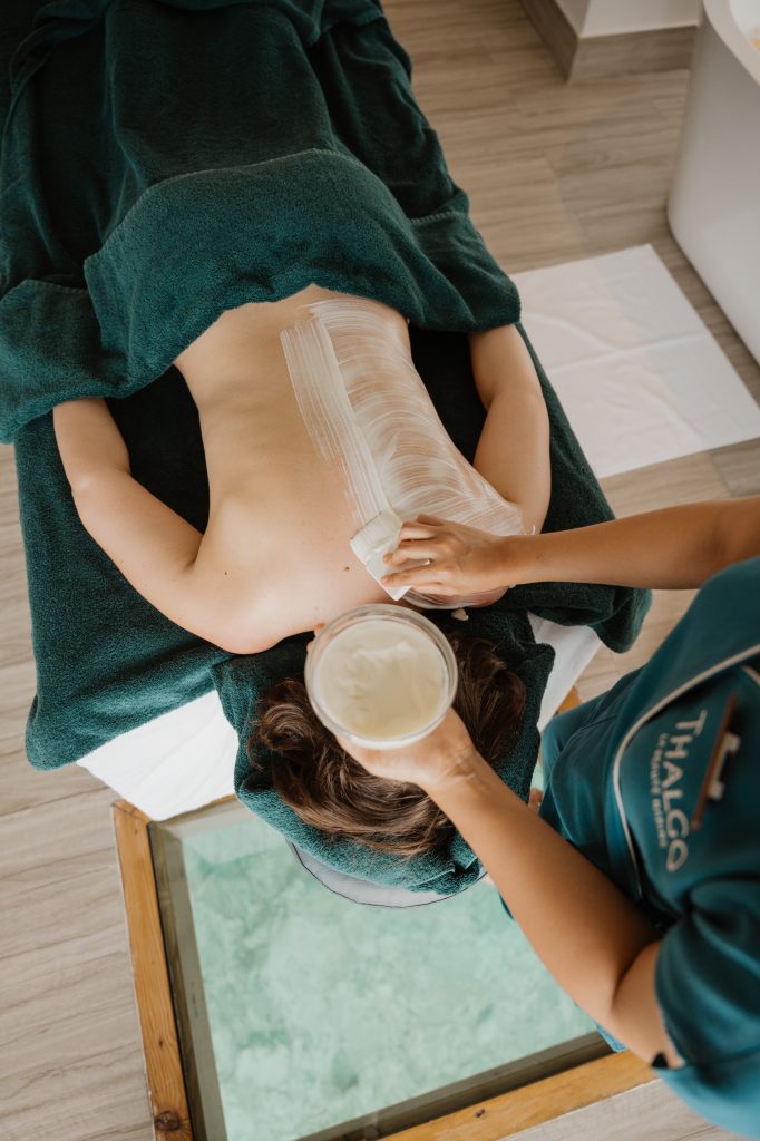 Frau liegt auf Bauch auf Massageliege und erhält Rückenbehandlung mit Creme durch eine zweite Person