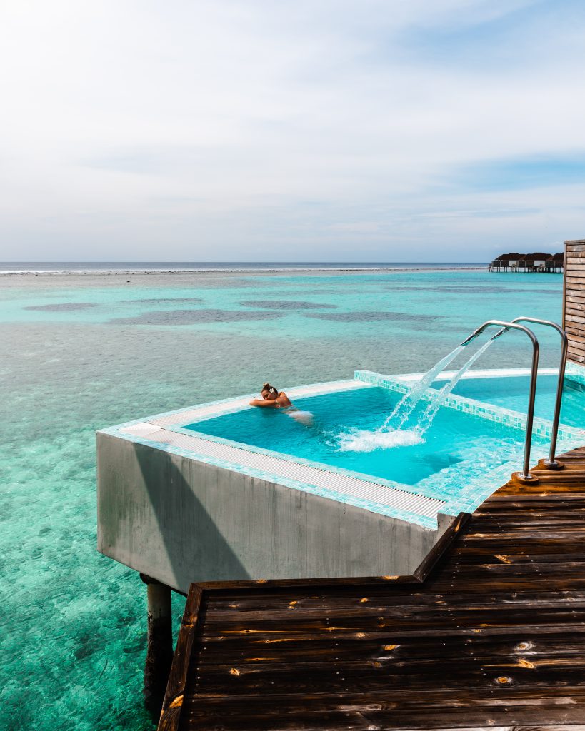 Infinity-Pool mit Wasserdüsen auf Holzsteg über türkisfarbenem Meer mit weiter Meeres- und Himmelssicht