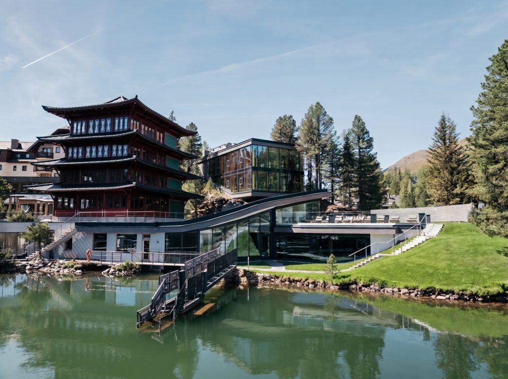 Außenaufnahme eines modernen Spa-Gebäudes mit asiatisch inspiriertem mehrstöckigem Teil neben einem Teich und einer grünen Wiese
