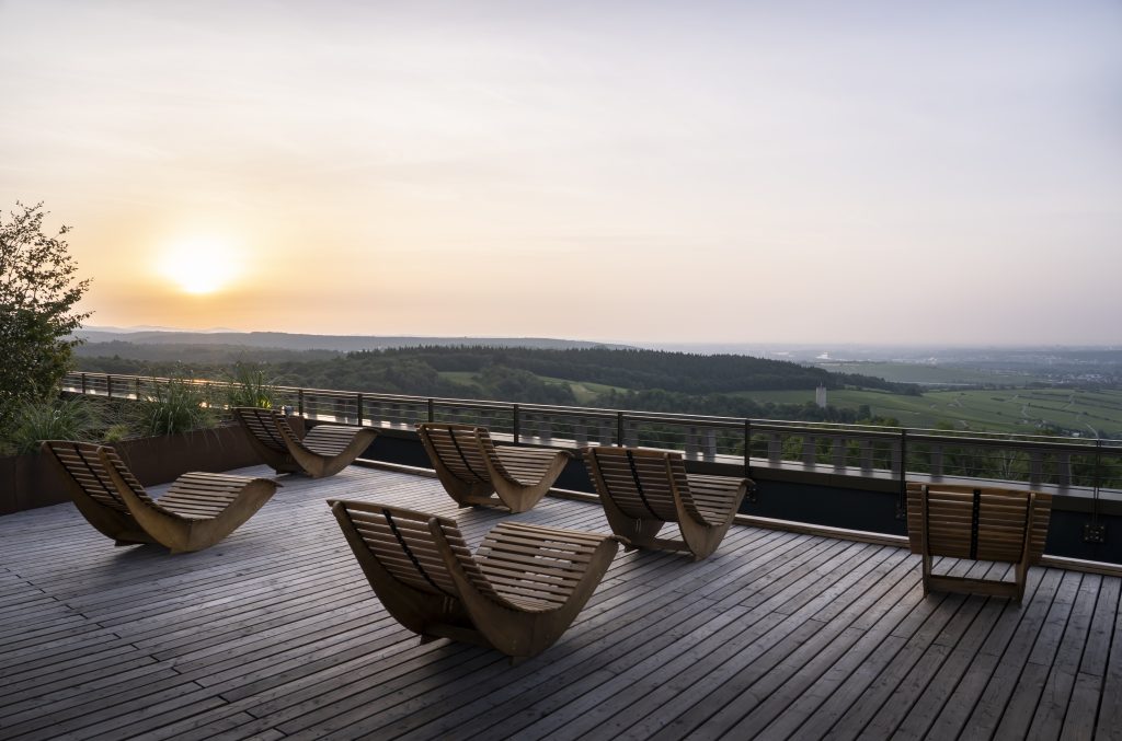 Holzterrasse mit geschwungenen Liegestühlen und Blick auf eine weite Landschaft bei Sonnenuntergang